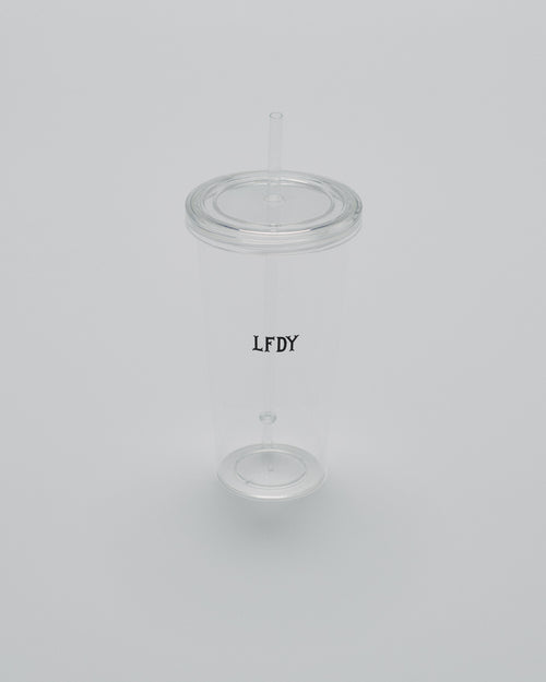 The LFDY Cold Cup by LIVE FAST DIE YOUNG is a clear plastic tumbler with a transparent lid and straw, featuring vertical black LFDY text on the side. Photographed on a plain light gray background. Berlin Store Exclusive.