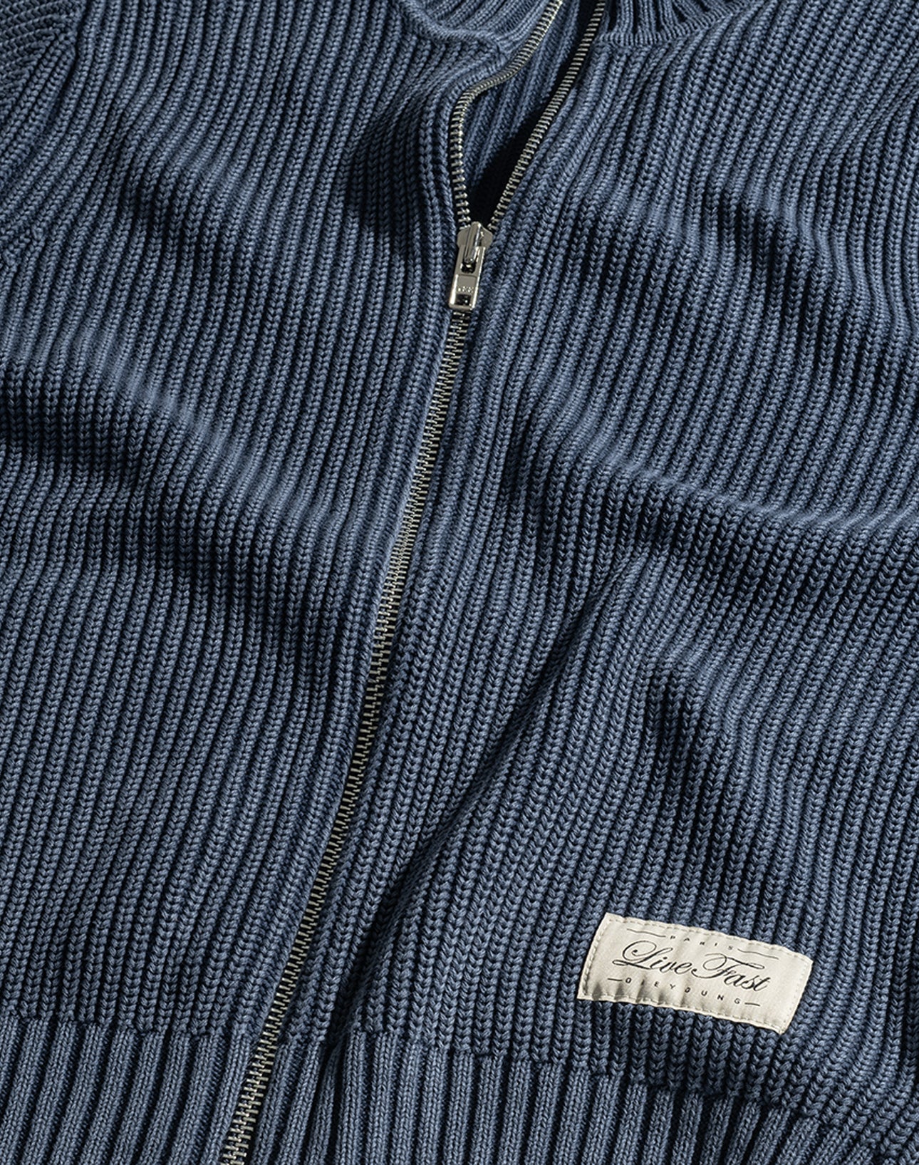 A close-up of the LFDY Knit Jacket by LIVE FAST DIE YOUNG shows a blue ribbed zip-up sweater with a Stehkragen, metal zipper, and a sewn-on white label reading "Inter Tradi Classic.