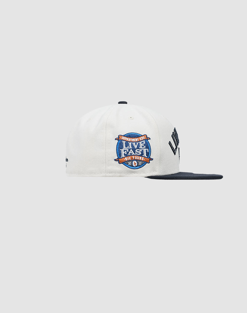 The LIVE FAST DIE YOUNG x NEW ERA 59FIFTY fitted cap in white and navy features a side-embroidered LFDY patch, shown on a plain gray background. Check the Größentabelle for perfect sizing.