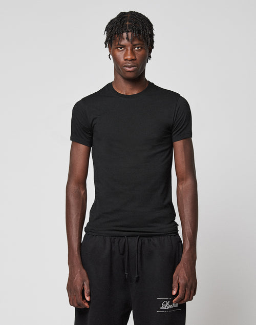 A young man with short, twisted hair wears the LFDY Slim Tee from LIVE FAST DIE YOUNG and black sweatpants, standing against a light gray background with a neutral expression.