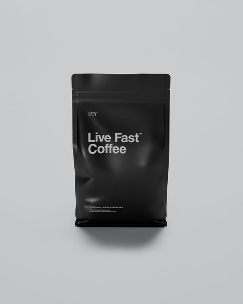 A matte black resealable coffee bag stands upright against a light gray background, labeled LIVE FAST COFFEE by LIVE FAST DIE YOUNG. The bag contains a quality blend of Arabica & Robusta whole beans.