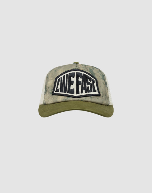 The LFDY Patched Trucker by LIVE FAST DIE YOUNG is a green and beige tie-dye cap with a curved brim, a bold black and white LIVE FAST patch on the front, and an adjustable Snapverschluss for the perfect fit.