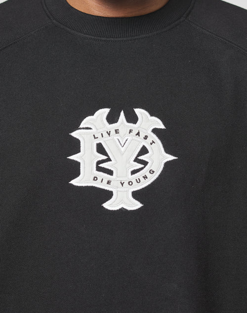 The DY Sweater by LIVE FAST DIE YOUNG is a black oversized sweatshirt with raglan sleeves, featuring a large white embroidered LY emblem and LIVE FAST DIE YOUNG in a circular chest design.