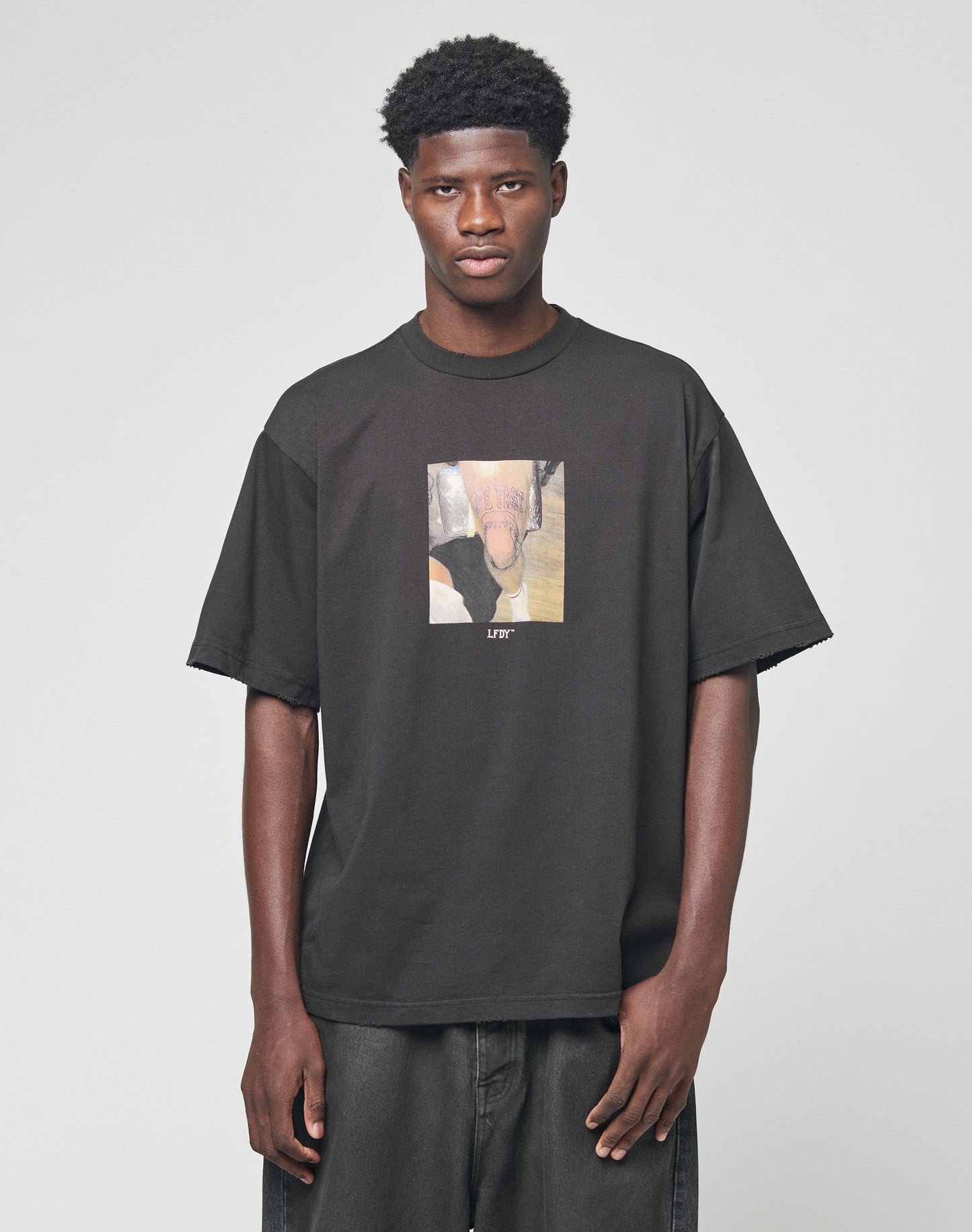 A person stands facing forward in the LFDY Sharkhunter Tee by LIVE FAST DIE YOUNG, an oversize black cotton t-shirt with a graphic of a horse’s nose and the word LIFT below, paired with dark jeans against a plain light background.