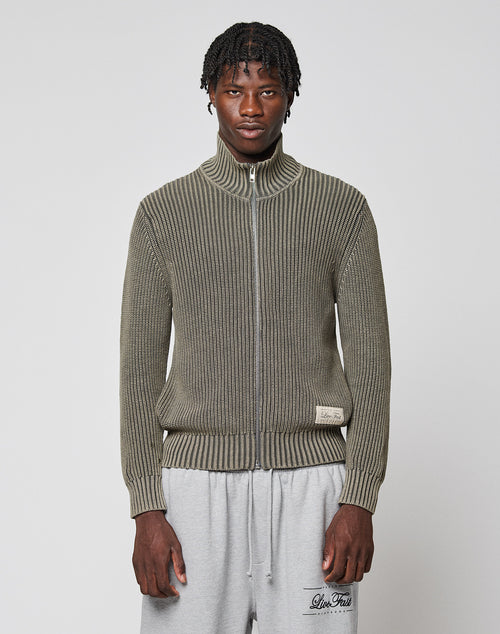 A man with short twisted hair wears the LFDY Knit Jacket from LIVE FAST DIE YOUNG in olive green and light gray sweatpants, standing against a plain white background.