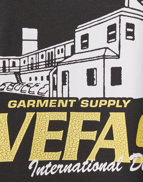 The LFDY Supply Tee by LIVE FAST DIE YOUNG features a building illustration with parked cars, GARMENT SUPPLY in yellow, and partial VEFA and International D as front and back prints on premium cotton in an oversized fit.