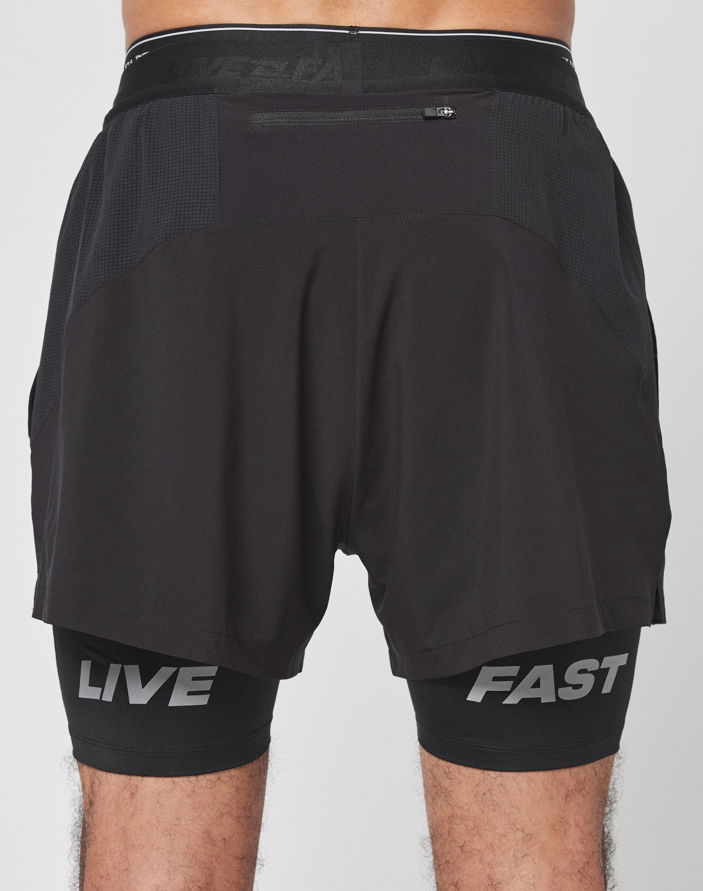 Back view of a person in black Live Fast Performance Running Shorts by LIVE FAST DIE YOUNG, featuring integrated tights with bold LIVE FAST branding in large gray letters on each leg, combining regular fit comfort and sporty style.