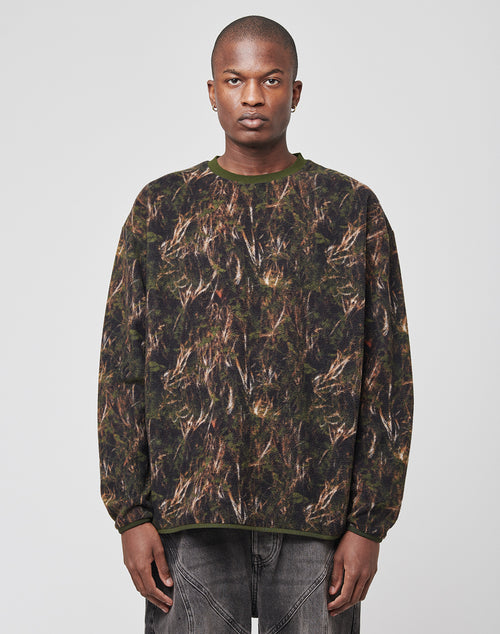 A person with a neutral expression wears the LFDY Fleece Longsleeve by LIVE FAST DIE YOUNG, featuring a green and brown camouflage-style abstract pattern, paired with faded gray jeans against a plain light background.