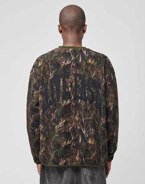 A person with a shaved head is seen from behind in an oversize LFDY Fleece Longsleeve by LIVE FAST DIE YOUNG, featuring a camouflage print and bold LIVE FAST lettering on the back. The setting is plain with a light background.