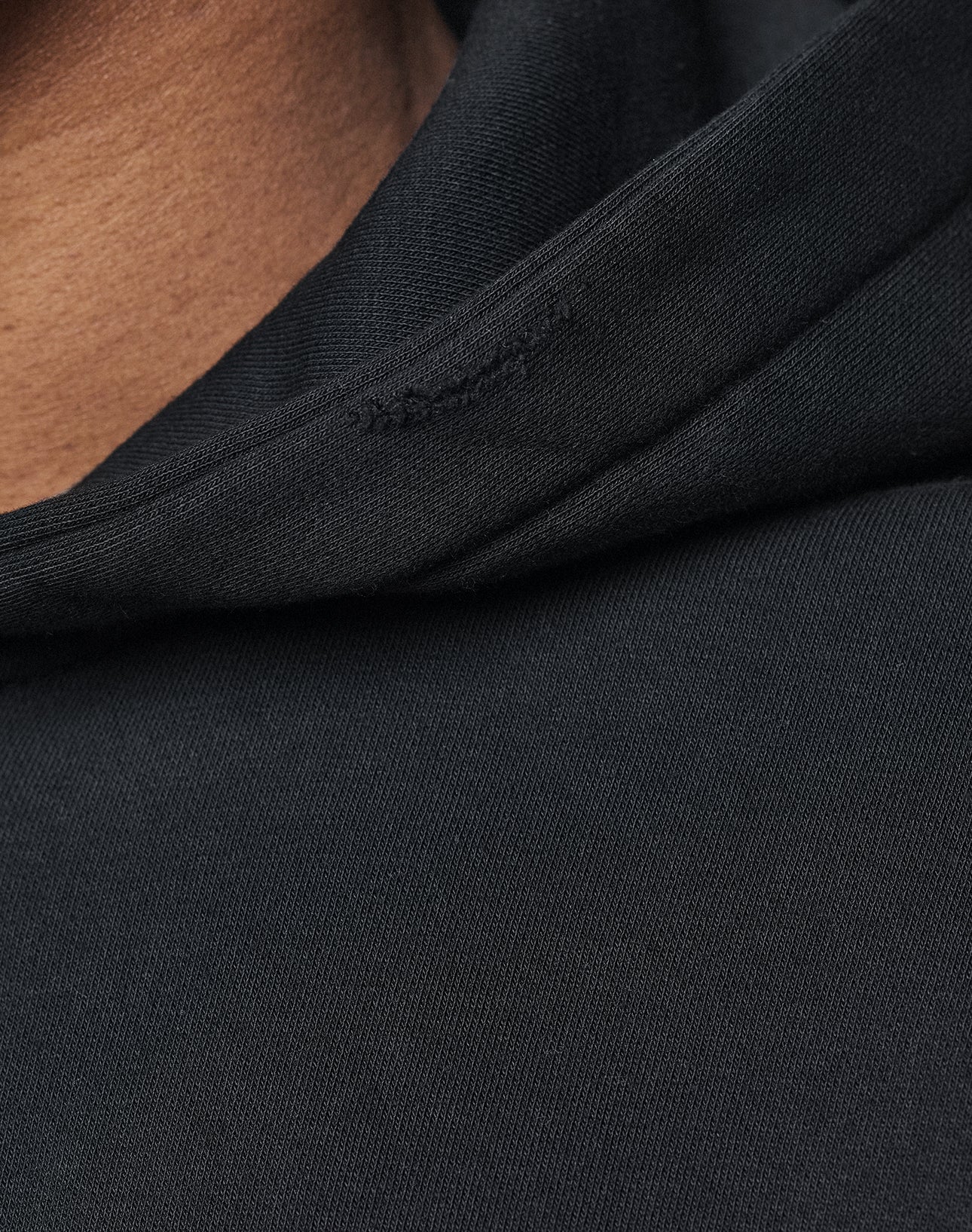Close-up of a person wearing the LIVE FAST DIE YOUNG Basic Hooded Zip in black. Only part of the hood and neck is visible, showcasing the fabric texture and stitching details.