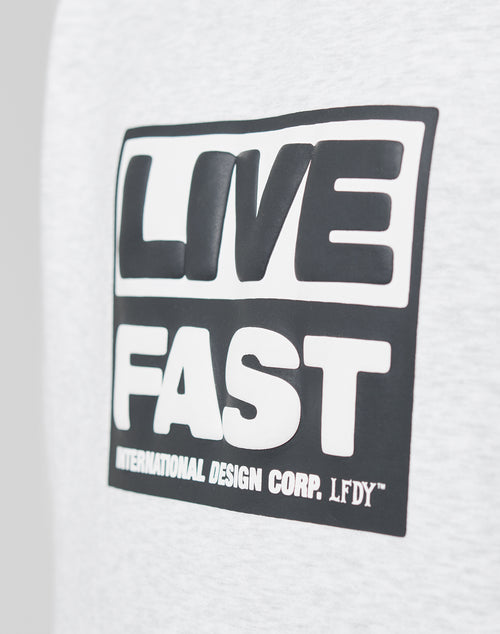 A close-up of the gray Live Fast Box Hooded by LIVE FAST DIE YOUNG, featuring an oversized fit and a black and white LIVE FAST puffer print, with INTERNATIONAL DESIGN CORP. LFDY⢠below and a subtle flag-label detail.