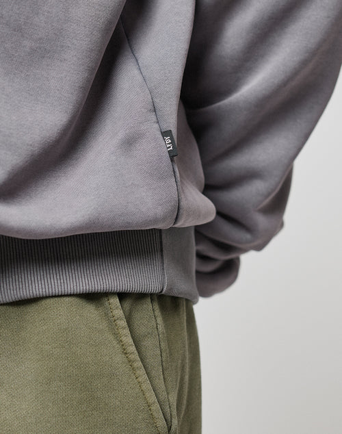 Close-up of a person wearing the LIVE FAST DIE YOUNG Basic Blank Hooded in gray Baumwolle Polyester with a small black icon tag, paired with olive green pants. Focus is on the side and waist of the sweatshirt.