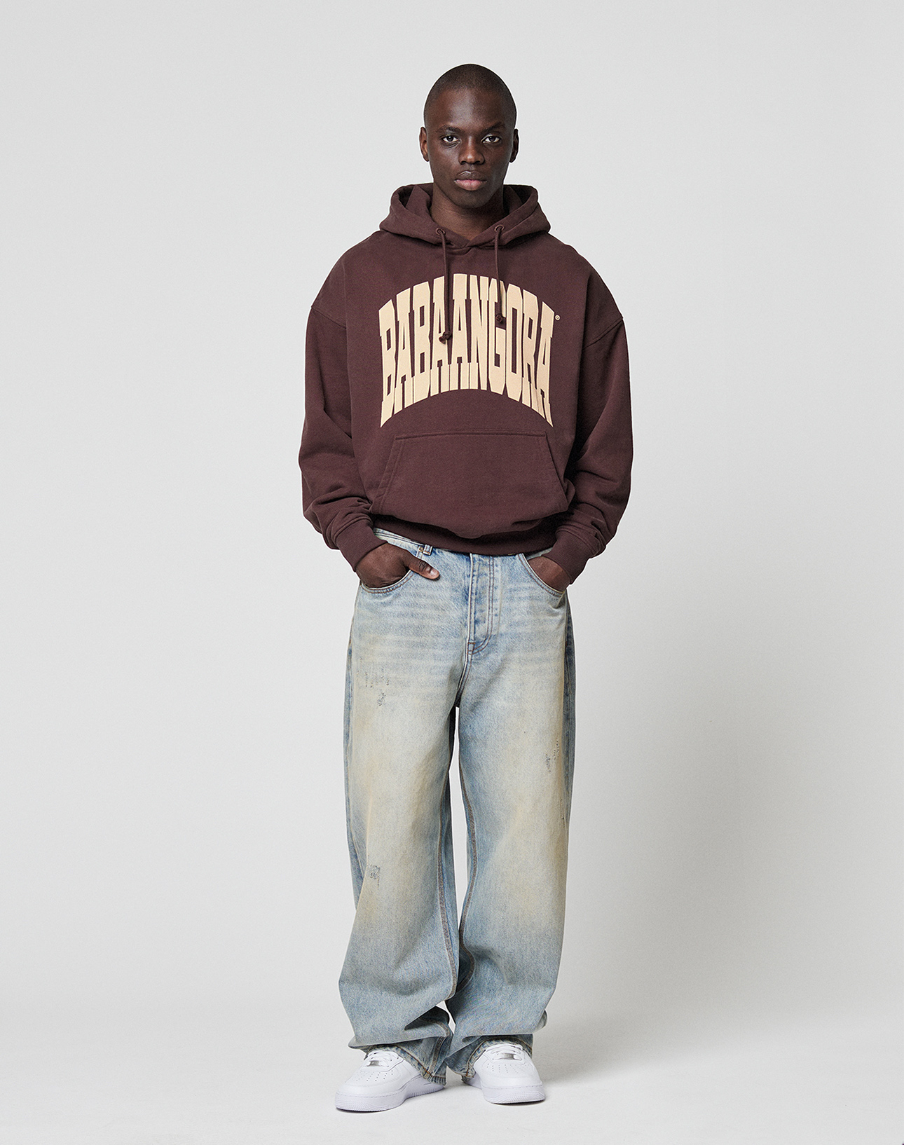 A person stands against a plain background wearing the LFDY x Baba Angora Hoodie by LIVE FAST DIE YOUNG, light blue baggy jeans, and white sneakersāa perfect streetwear look inspired by Berliner Stiftung style.