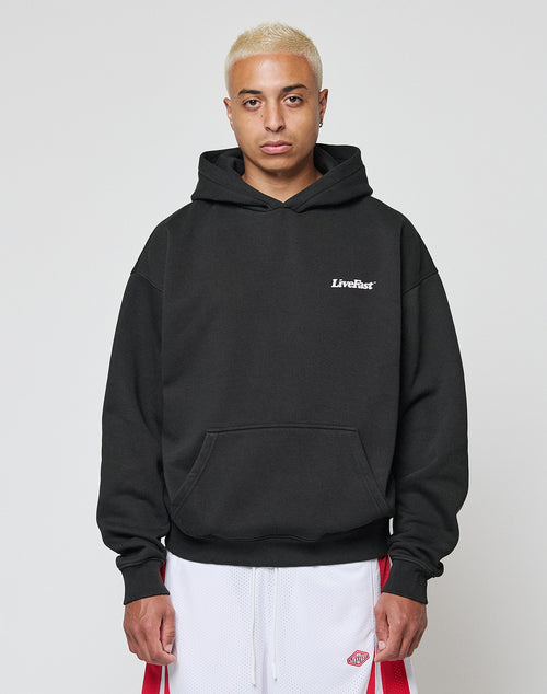 A person with short blond hair wears the LIVE FAST DIE YOUNG Basic 360 Hooded in black with white chest print, paired with white athletic shorts with red stripes, standing against a plain white background.