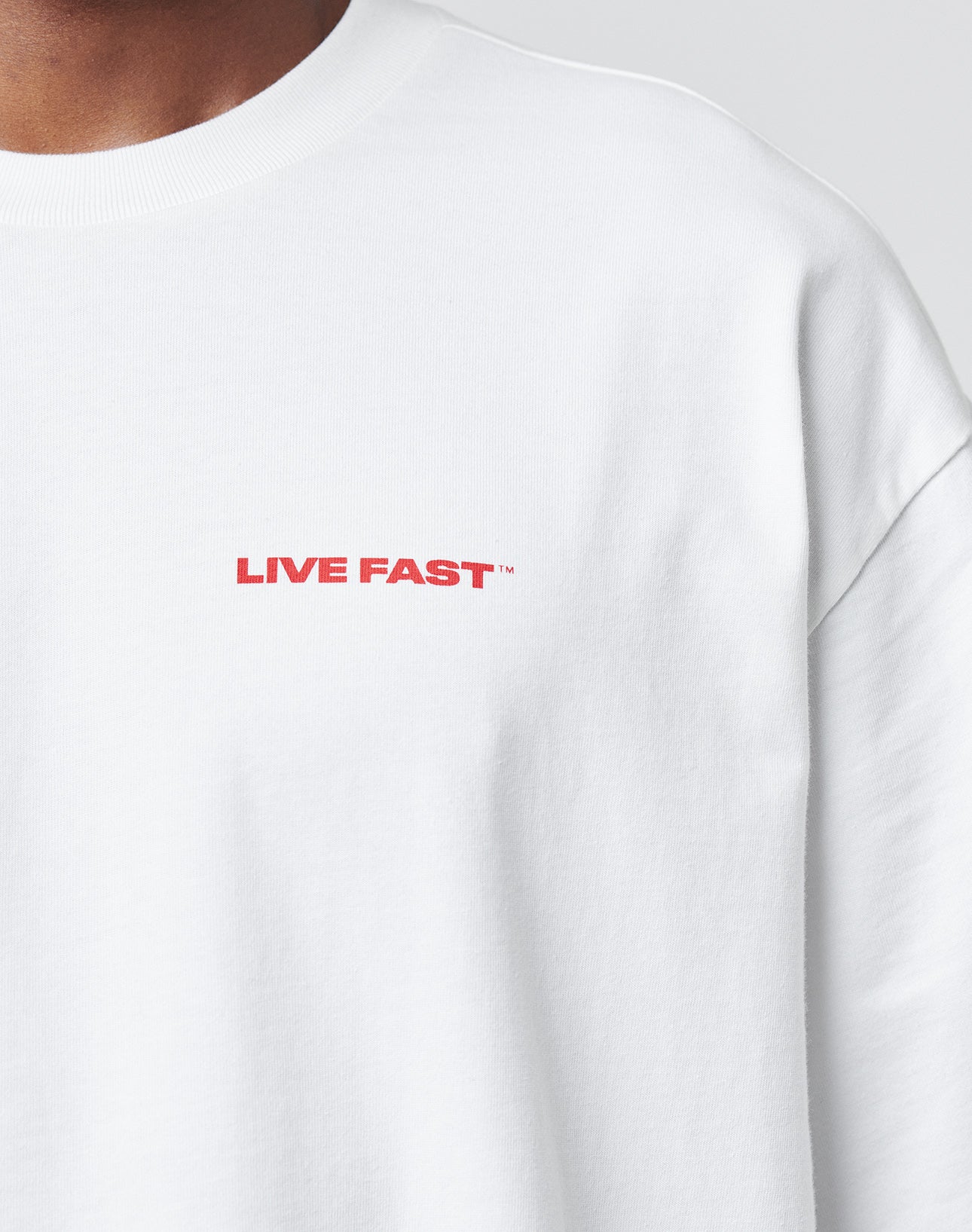 Close-up of a person wearing the LFDY Cinema Tee by LIVE FAST DIE YOUNGāan oversize white sweatshirt with LIVE FAST in bold red on the upper left chest. Crafted from 100% Baumwolle for superior comfort and style.