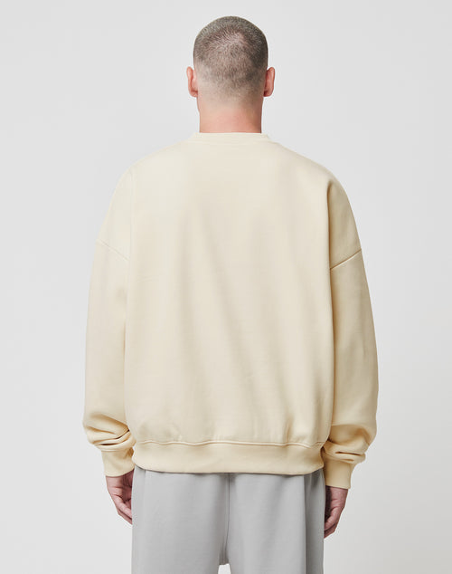 A person with short hair is seen from behind, wearing a loose, light beige Basic Blank Sweater by LIVE FAST DIE YOUNG and light gray pants, standing against a plain white background.