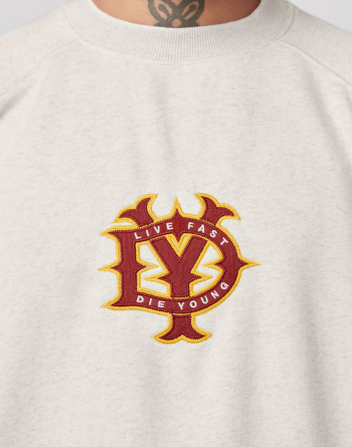 A close-up of the light gray DY Sweater by LIVE FAST DIE YOUNG shows topstitching and a red and yellow embroidered brand emblem in a stylized design. The wearers tattooed neck is visible above the collar.