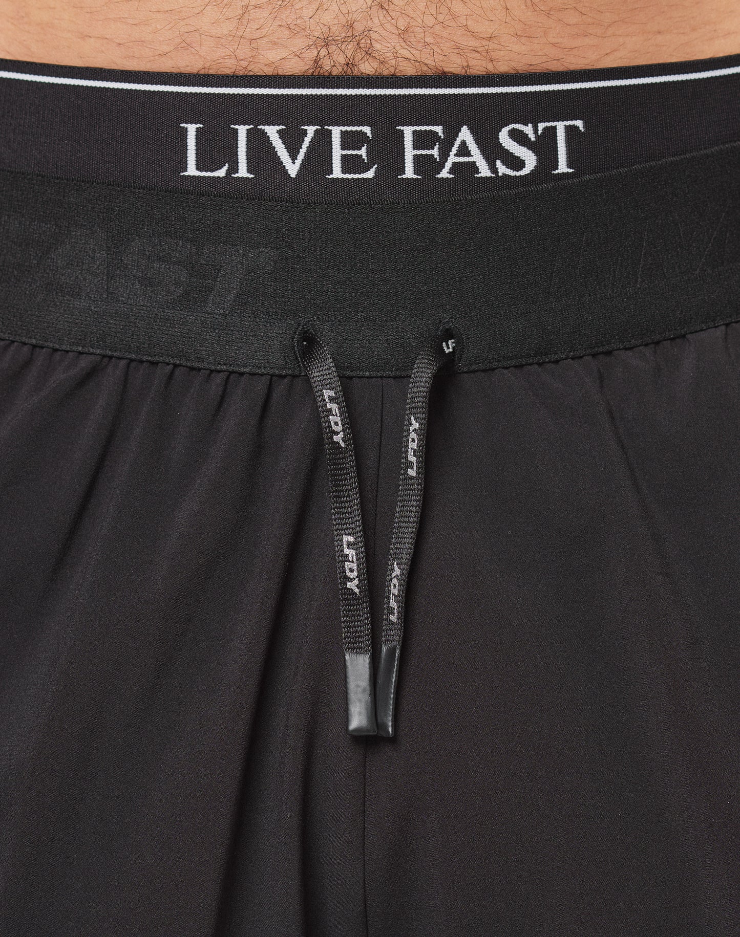 Close-up of a waist wearing LIVE FAST DIE YOUNGs Live Fast Performance Shorts in black, featuring an elastic waistband with LIVE FAST lettering and black drawstrings with white text. Regular Fit offers comfort and style.