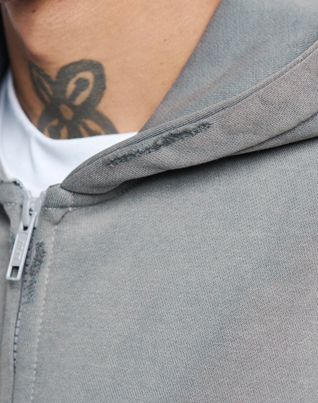 Close-up of a person wearing the LIVE FAST DIE YOUNG Basic Hooded Zip in light gray over a white shirt, showing part of a black floral neck tattoo above the collar.