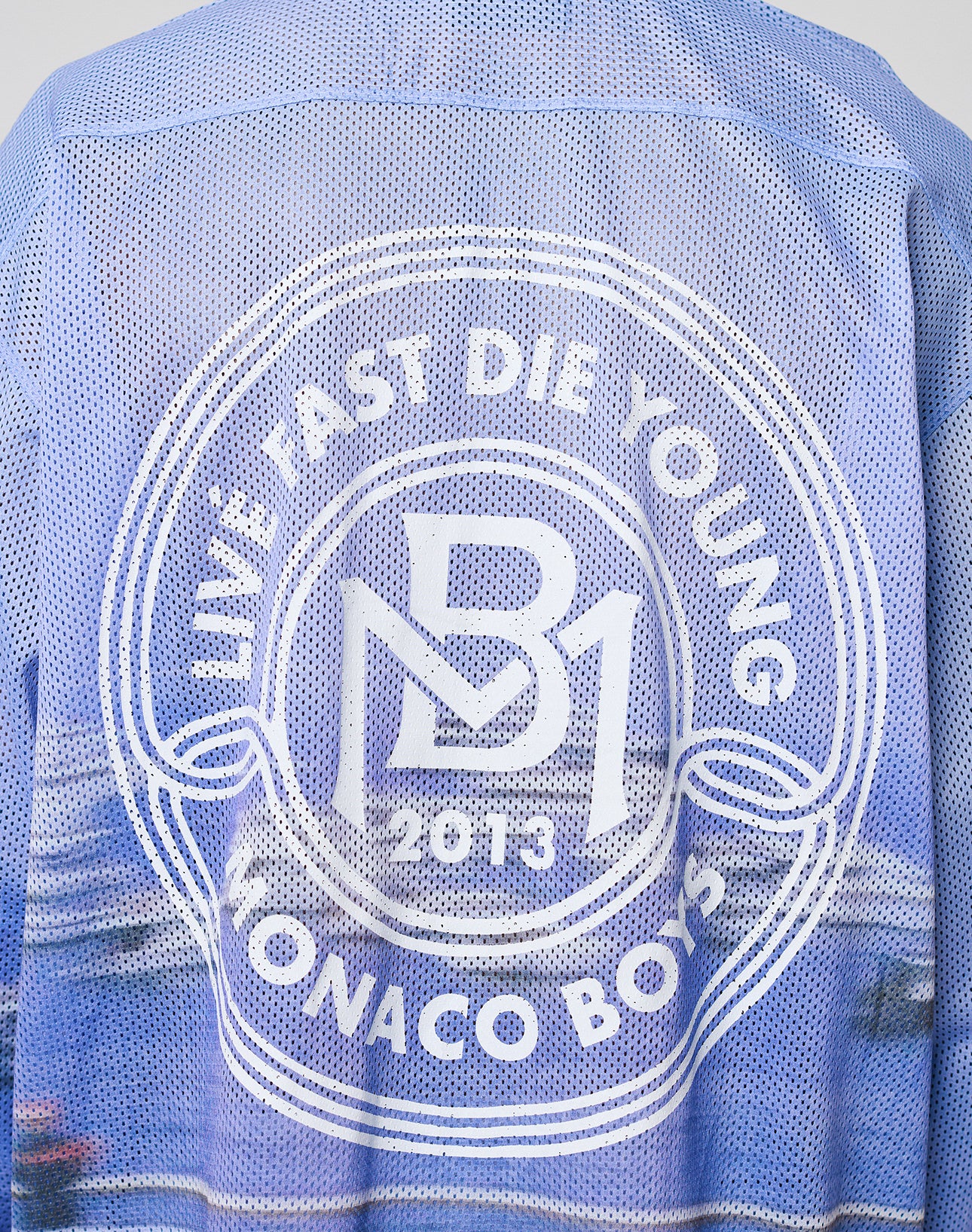 A close-up of the LFDY Yacht Jersey by LIVE FAST DIE YOUNG, a blue mesh oversized jacket with a white circular back logo reading LIVE FAST DIE YOUNG, MB1 2013, MONACO BOYS. Made from 100% polyester.