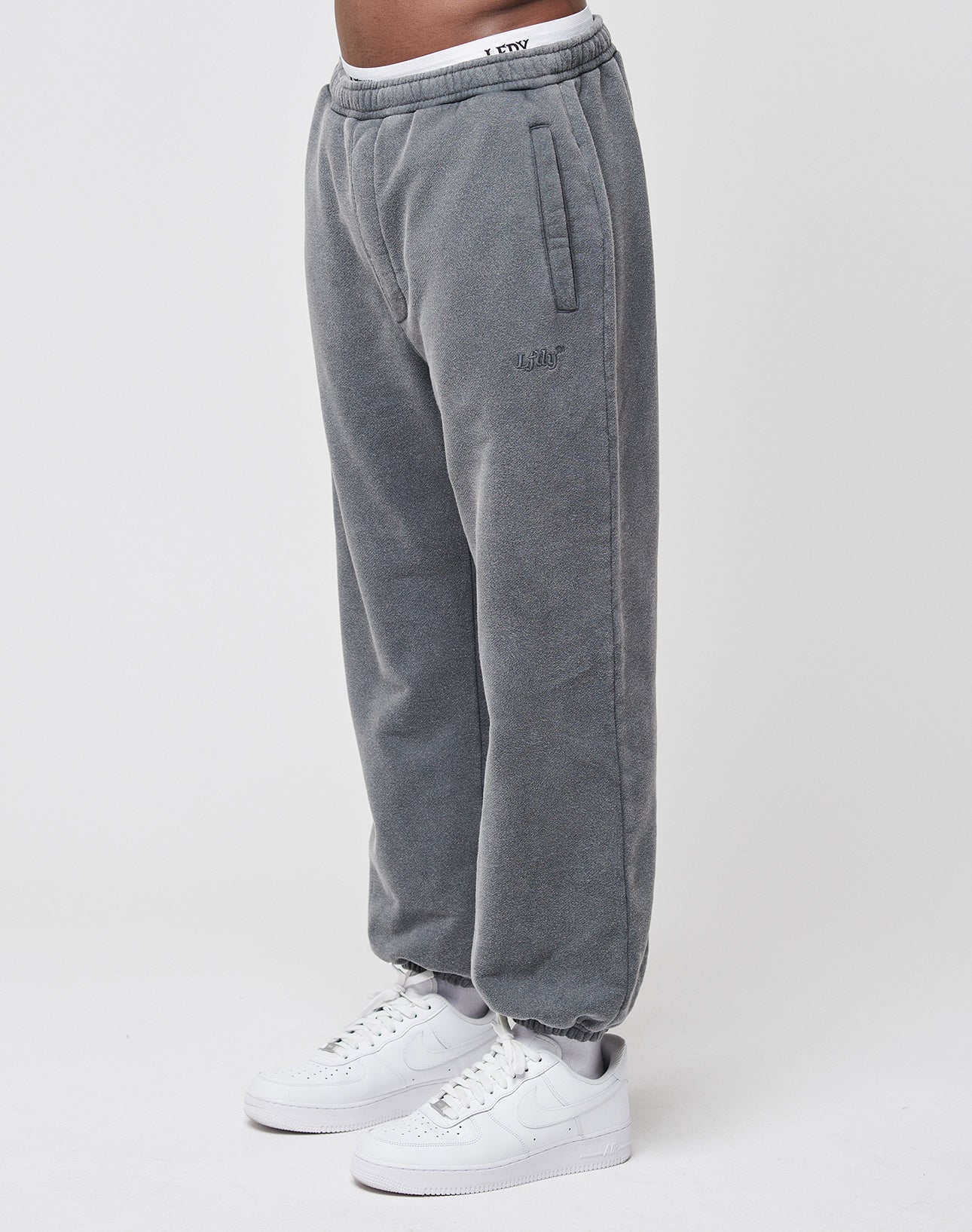 A person wears LIVE FAST DIE YOUNG Loose Jogger sweatpants in grey with Elastik-Bund and side pockets, paired with white sneakers. Only the lower half is visible against a plain white background.