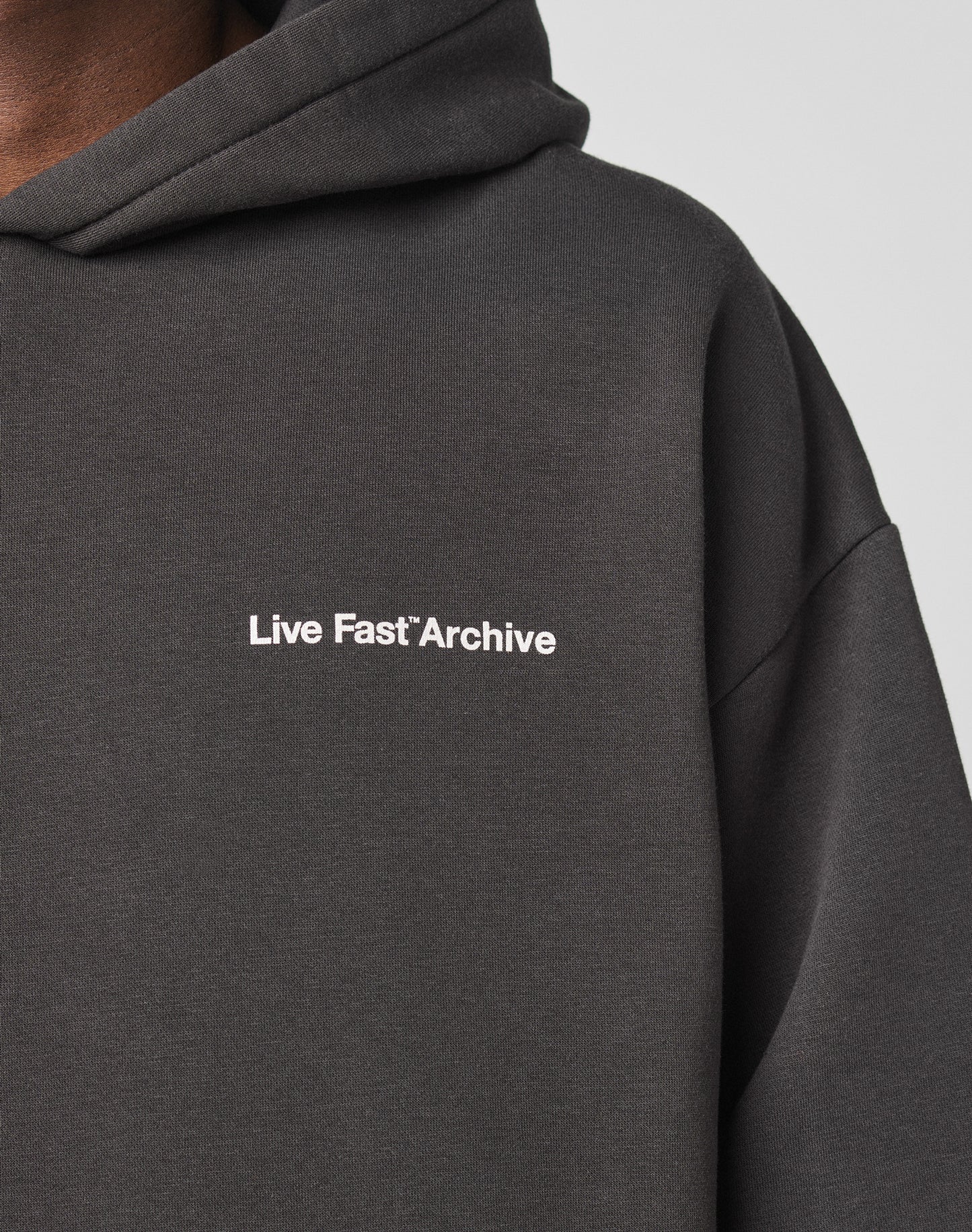 A close-up shows a person in the LIVE FAST DIE YOUNG LFDY Middlefinger Hooded, an oversize fit dark hoodie with Live Fast*Archive in small white letters on the chest. The lower face and neck are partially visible.