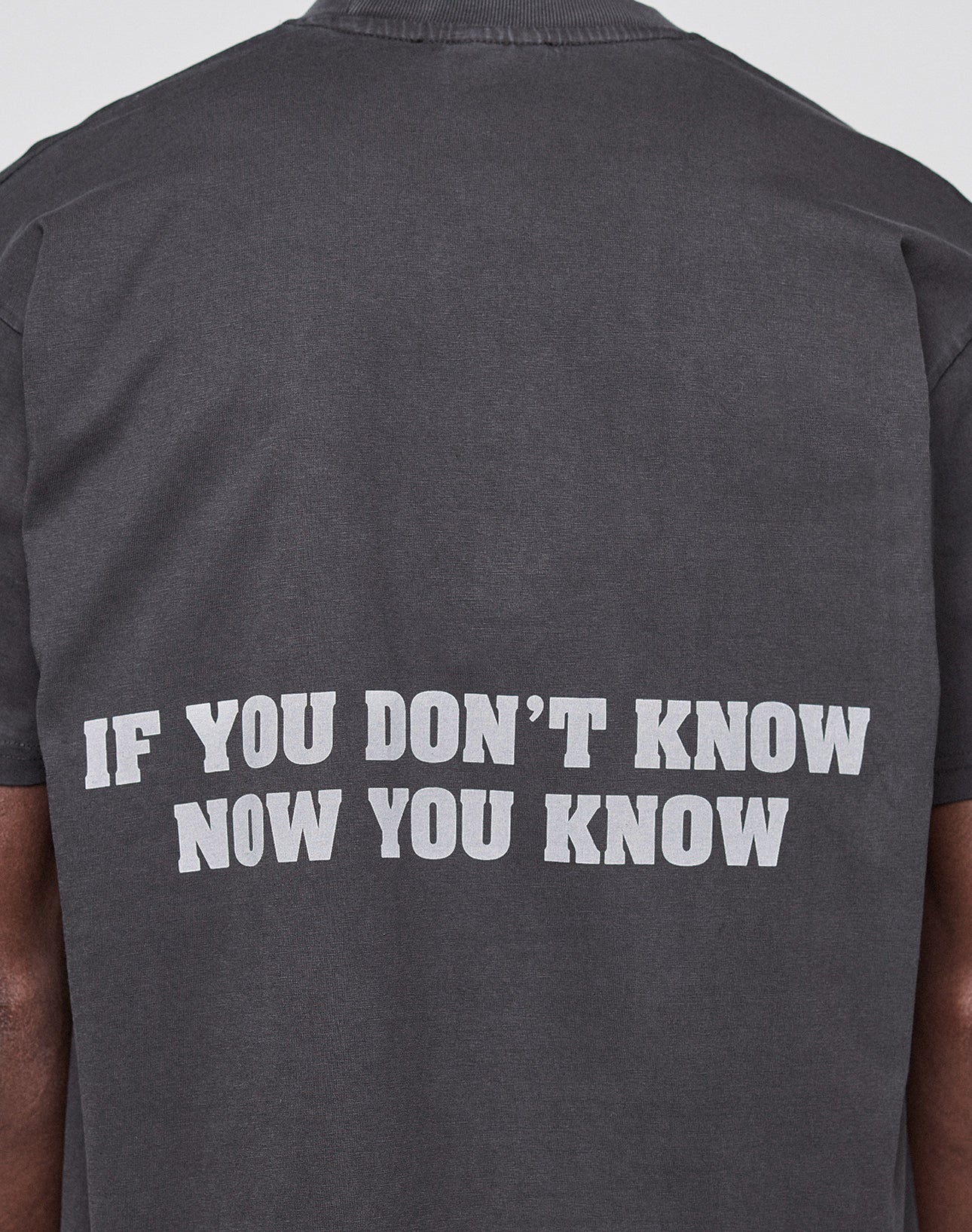 Someone is wearing the Abus Magomedov Tee by LIVE FAST DIE YOUNG—a dark gray Regular Fit shirt made from 100% Baumwolle, featuring bold white "IF YOU DONT KNOW NOW YOU KNOW" text across the back.