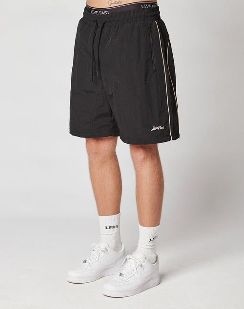 A person wearing LIVE FAST DIE YOUNG Beach Shorts, white crew socks with LFDY text, and white Nike sneakers stands against a plain light background.