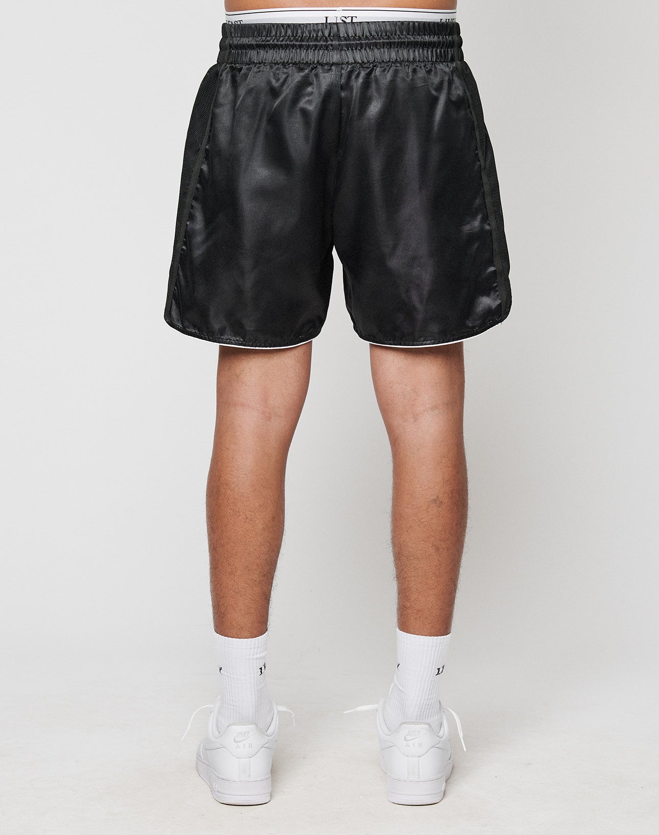 A person is shown from the waist down against a plain background, wearing LIVE FAST DIE YOUNG LFDY Fighting Shorts in black, paired with white crew socks and white sneakers.