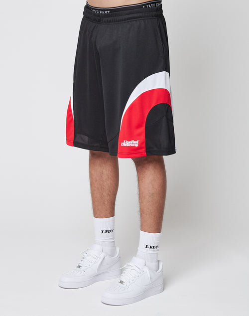 A person wearing LIVE FAST DIE YOUNG Basic Trackshorts in black with red and white curves, paired with white LEDY socks and white Nike sneakers, stands against a plain white background.