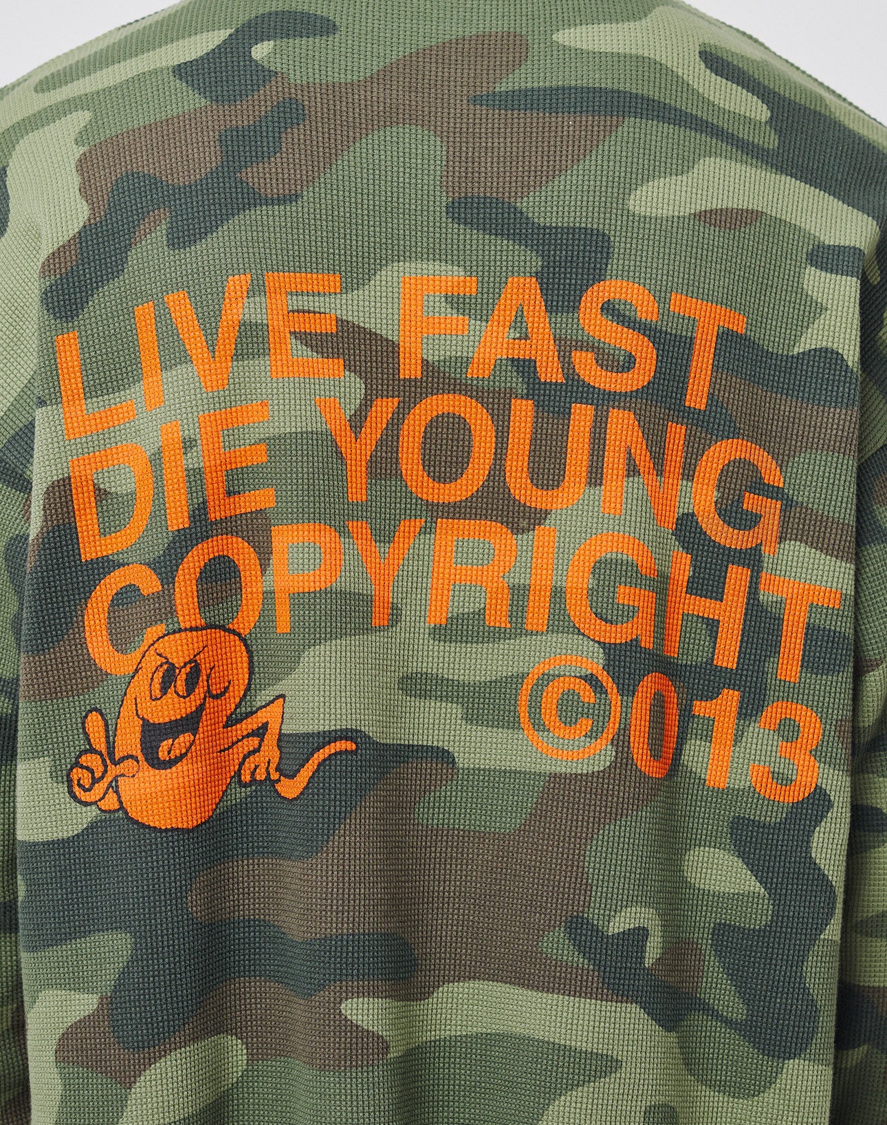 The LIVE FAST DIE YOUNG Copyright Waffle Longsleeve is a green camo oversize-fit top with bold orange text, cartoon hand-gesture graphic, striking backprint, and is made from 100% Baumwolle.