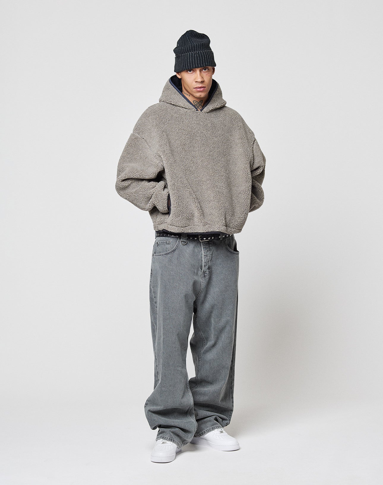 A person wearing the gray LFDY Teddy Hooded by LIVE FAST DIE YOUNG, baggy gray oversize jeans, a black beanie, and white sneakers stands against a plain white background with hands in pockets.
