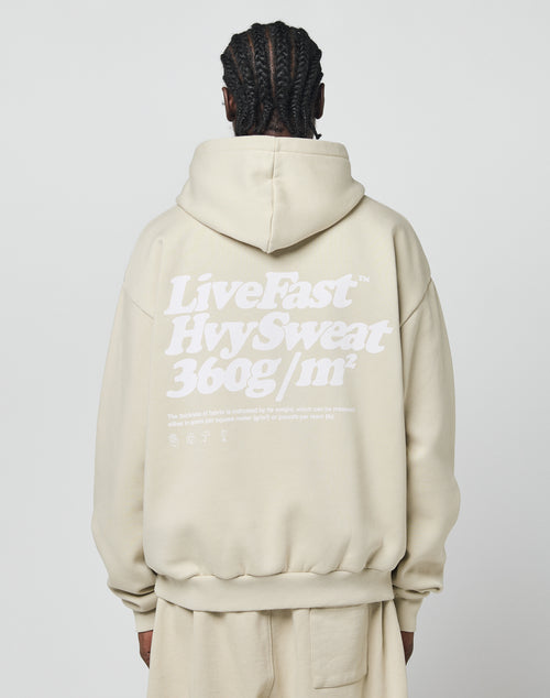 Seen from behind, a person with braided hair wears the Basic 360 Hooded by LIVE FAST DIE YOUNG—an oversize fit beige hoodie with bold white LiveFast HvySweat 360g/m² text and smaller details, crafted from premium cotton and polyester.