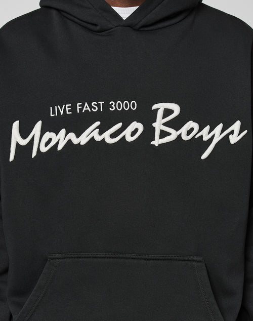 A person is wearing the LIVE FAST DIE YOUNG Monaco Boys Hooded black hoodie with white 3D Stick text. Made from a comfy Baumwolle-Polyester Mix, only the torso and part of the oversize-fit hood are visible.