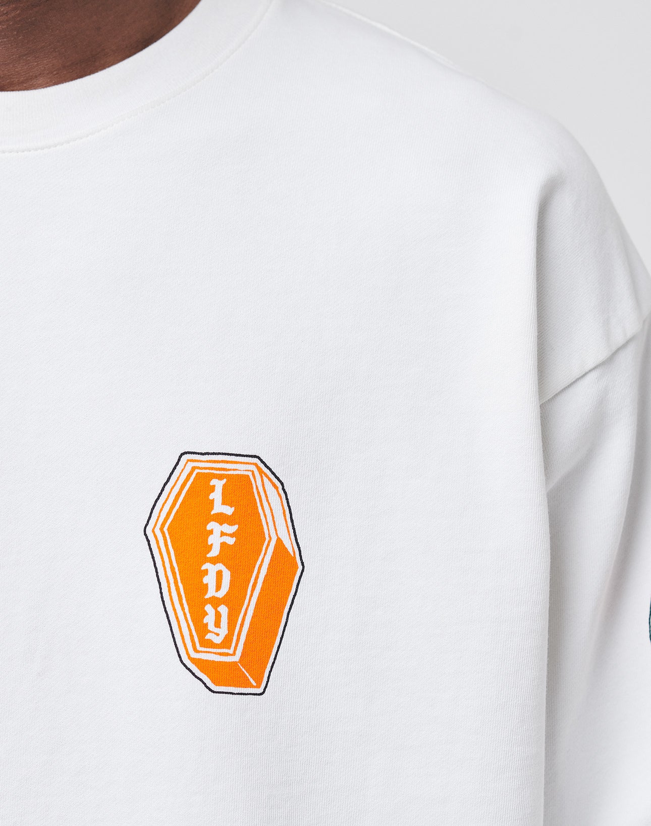 A close-up of the No Rich Parents Longsleeve by LIVE FAST DIE YOUNG, a white Regular Fit shirt featuring an orange coffin-shaped graphic with white LFDY lettering on the left chest.
