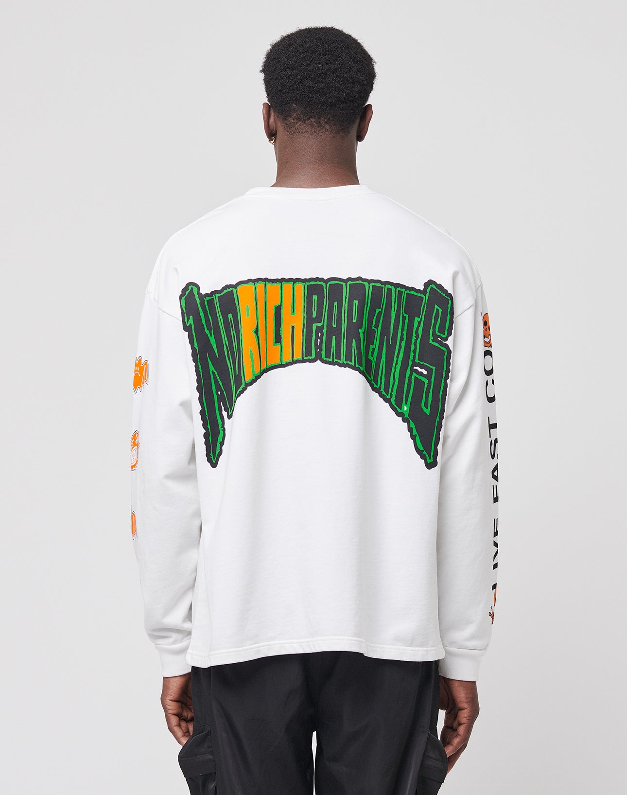 A person with short hair, seen from behind, wears the LIVE FAST DIE YOUNG No Rich Parents Longsleeveāa white French Terry Regular Fit shirt featuring bold green, yellow, and black NO RICH PARENTS text on the back and orange sleeve graphics.