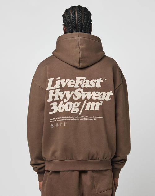 A person with braided hair, seen from behind, wears a brown Basic 360 Hooded hoodie by LIVE FAST DIE YOUNG. Bold white text and smaller print are on the back. The hoodie, made from a cotton-poly blend, is paired with matching brown pants.