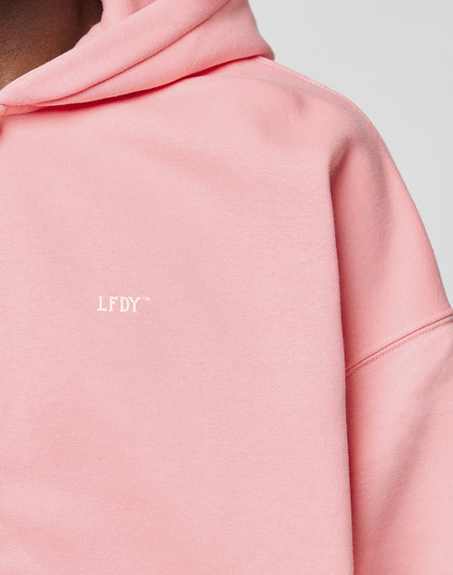 Close-up of a person wearing the Basic Hooded Zip by LIVE FAST DIE YOUNG in light pink, featuring a small white LFDY™ chest logo. The cropped fit shows part of the face, neck, shoulder, and upper chest for a sleek branded look.