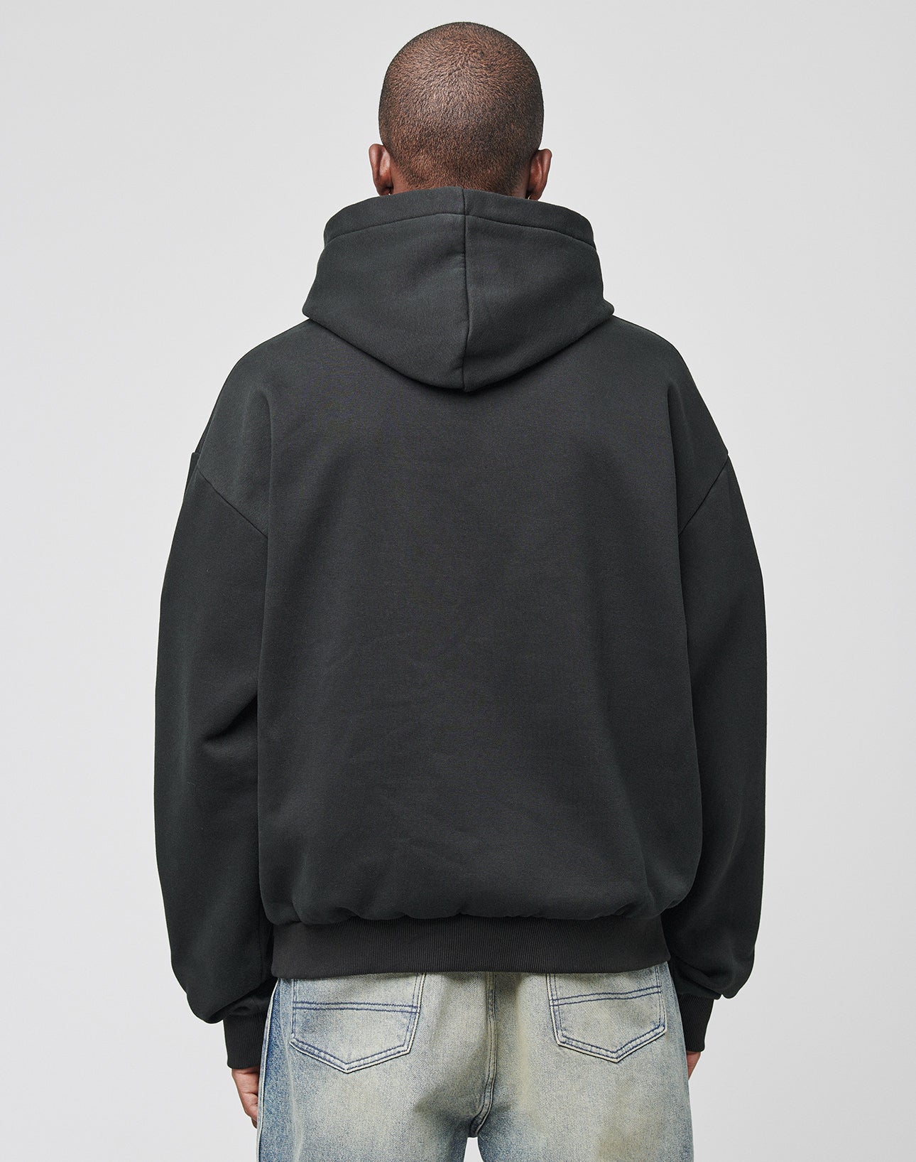 A person faces away from the camera, wearing a LIVE FAST DIE YOUNG Live Fast Tribal Hooded sweatshirt in black with light blue jeans, set against a plain gray background.