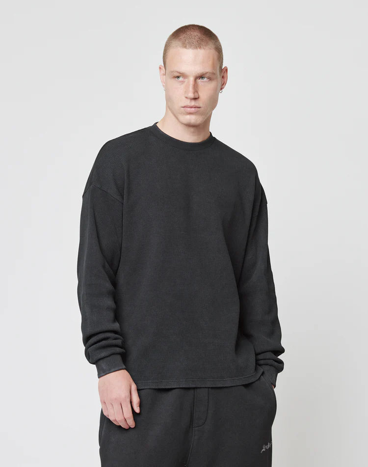 A young man with short blond hair wears the LIVE FAST DIE YOUNG Blank Waffle Longsleeve and matching black pants, both made from 100% Baumwolle, while standing against a plain light gray background.