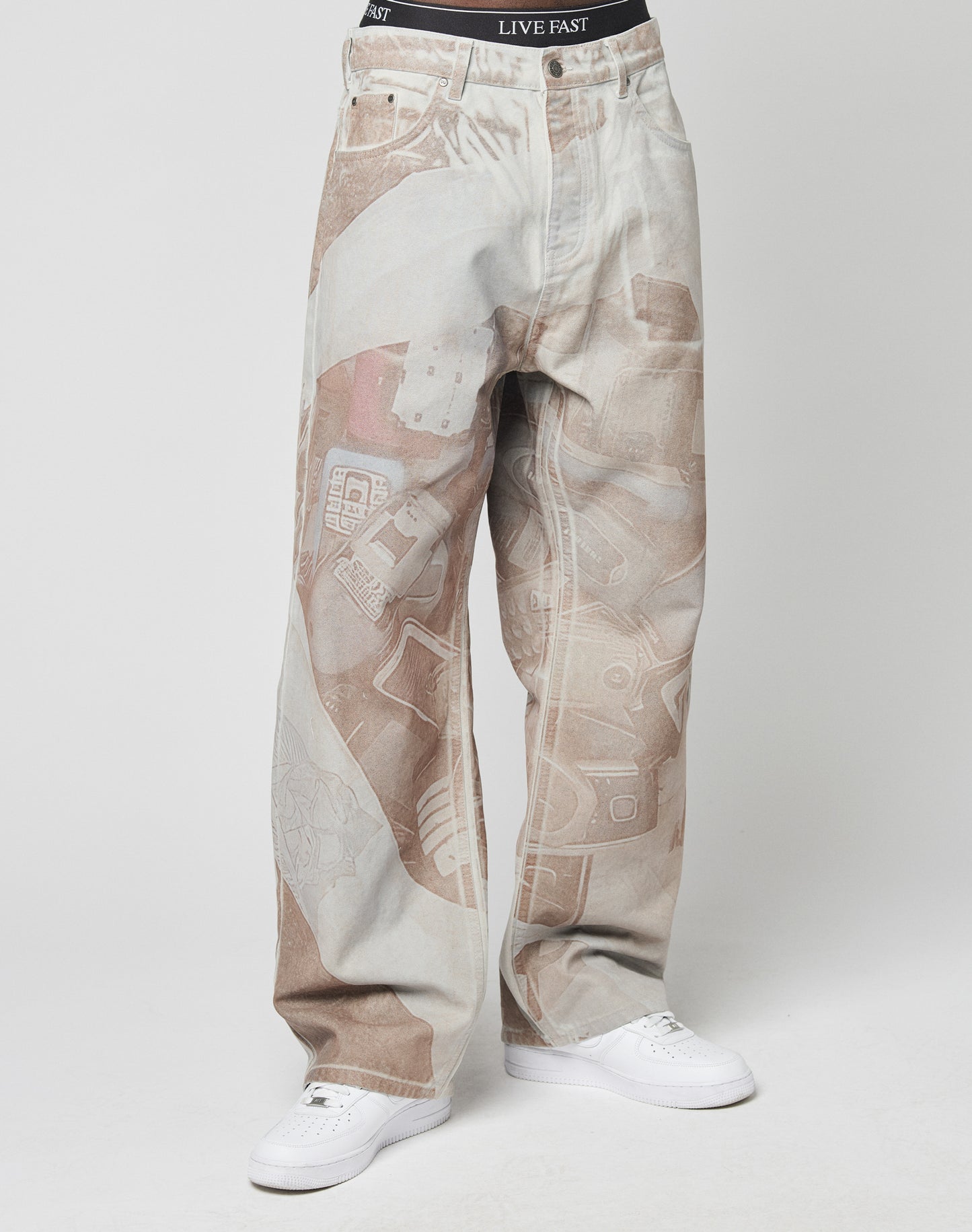 A person wears LFDY Stolen Phones Denim by LIVE FAST DIE YOUNGâbaggy fit, 100% cotton, brown and white abstract printâpaired with white sneakers. The waistband of black LIVE FAST underwear shows above the jeans.