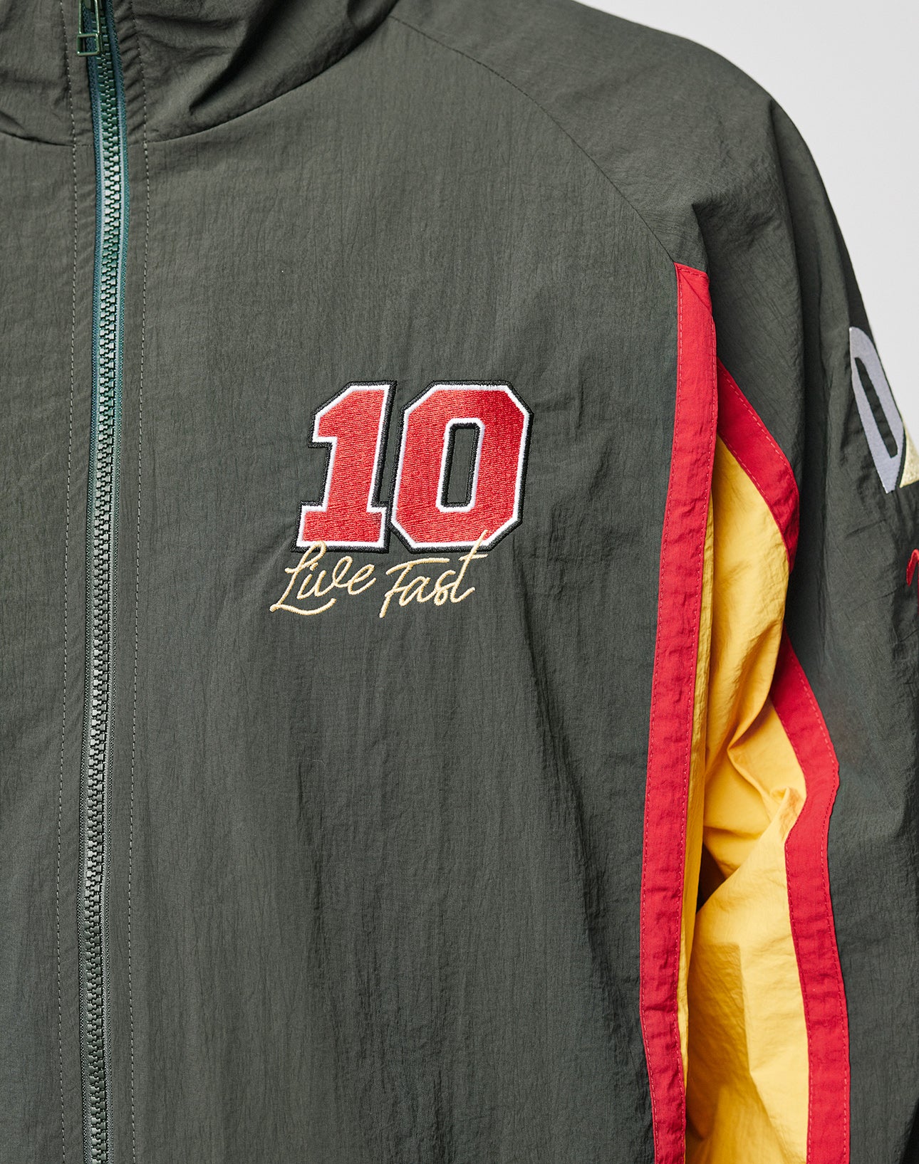 A close-up of the Westend Trackjacket by LIVE FAST DIE YOUNG, a dark green, regular fit jacket with red and yellow sleeve stripes, a red and white 10 patch on the chest above Live Fast embroidery, all in durable polyester.
