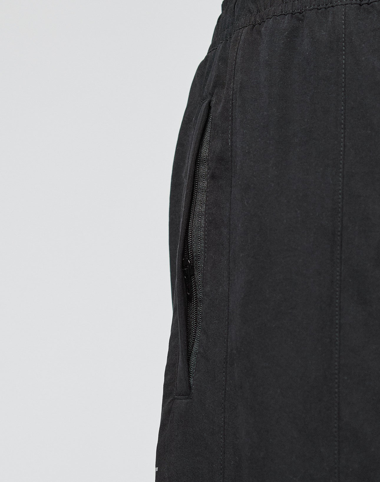 Close-up of the side pocket, waistband with elastikbund, and partially open zipper on black LFDY Trackpants by LIVE FAST DIE YOUNG. The background is plain light gray.