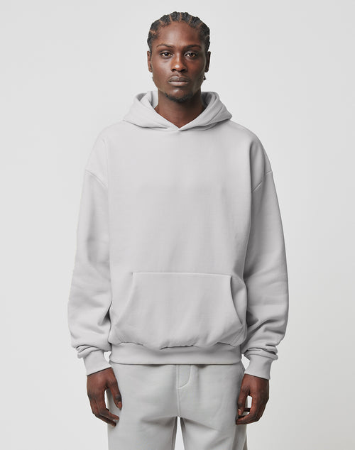 A person with braided hair faces forward, wearing the LIVE FAST DIE YOUNG Basic Blank Hooded in light gray and matching sweatpants made from soft Baumwolle and polyester, set against a plain, light background.