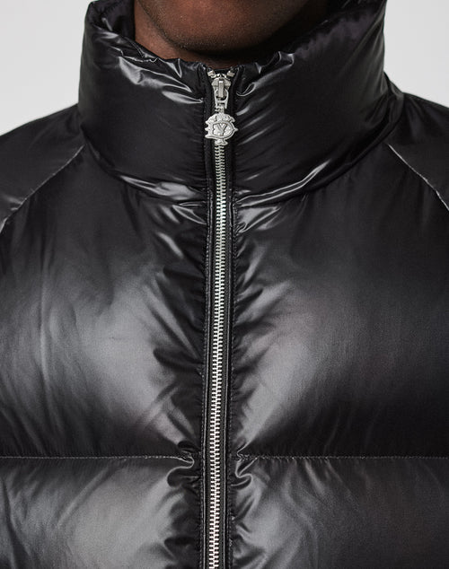 A close-up of a person wearing the Live Fast Down Jacket by LIVE FAST DIE YOUNG in shiny black, featuring a high collar and visible silver center zipper, designed to be water-repellent for extra protection.