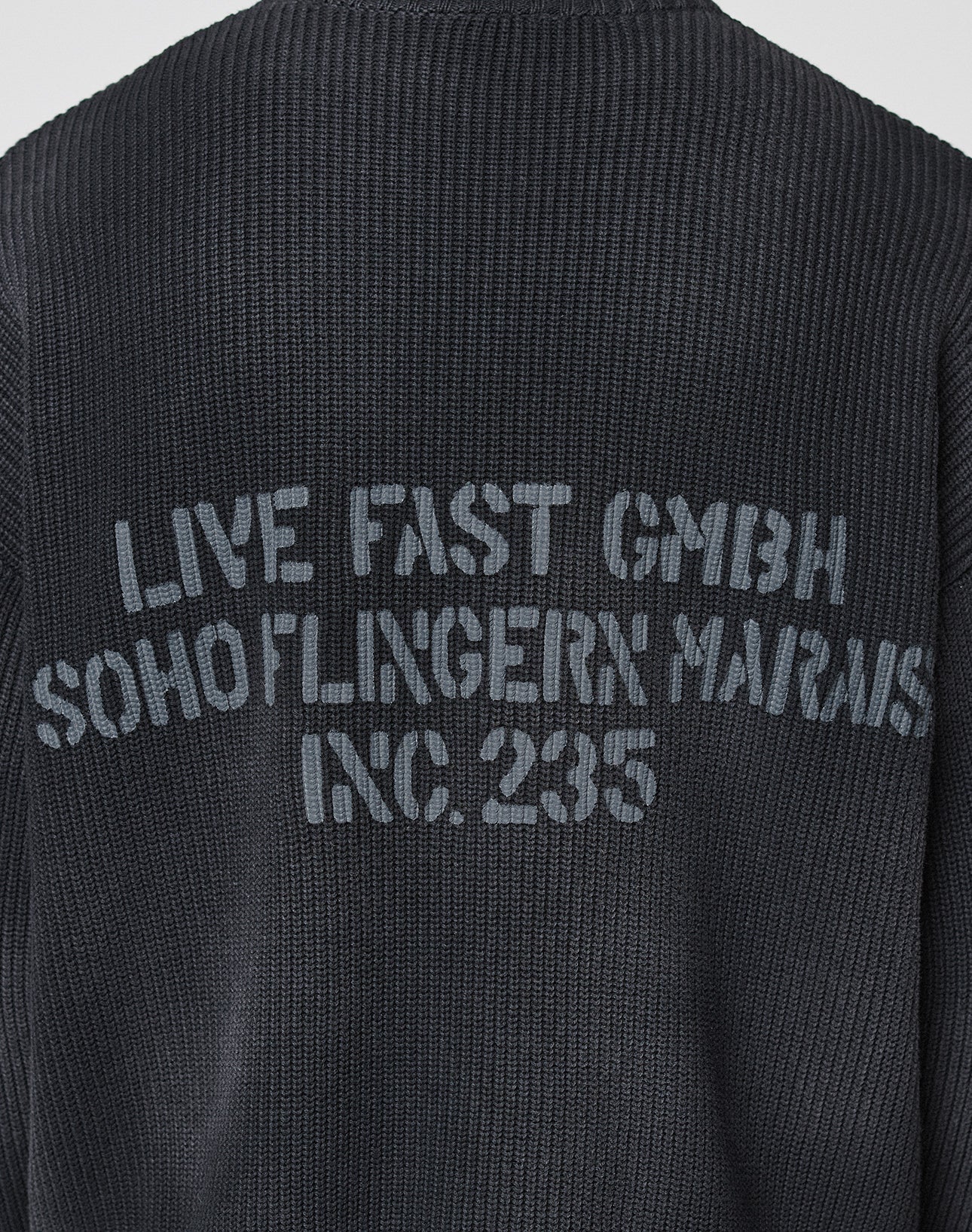 A close-up of the backprint on the black LFDY Washed Knit Sweater by LIVE FAST DIE YOUNG, featuring faded gray text and crafted from 100% Baumwolle for all-day comfort and style.