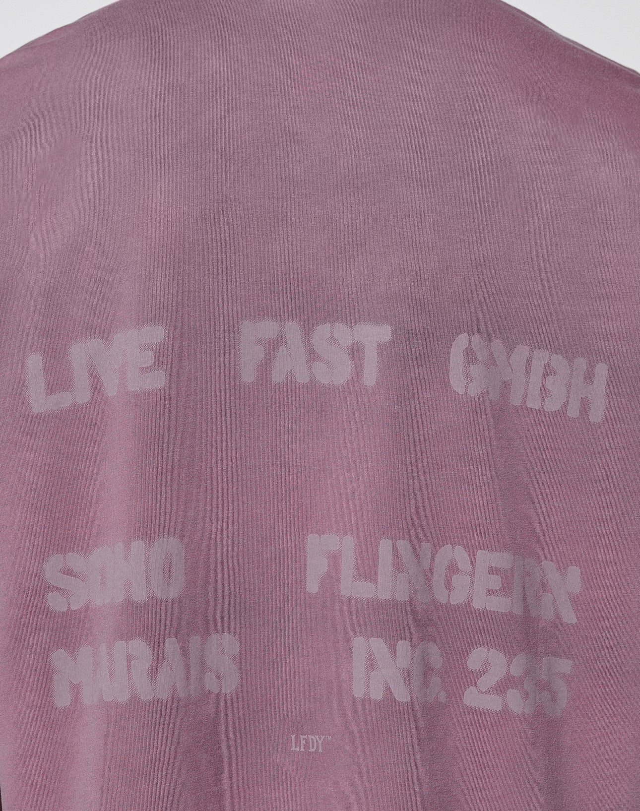 The Live Fast District Tee by LIVE FAST DIE YOUNG is an oversized mauve shirt with white stenciled text: LIVE FAST GMBH, SOHO, FLINGER, MARAIS, INC. 2355. Made from 100% Baumwolle, the fabric looks soft on a plain background.