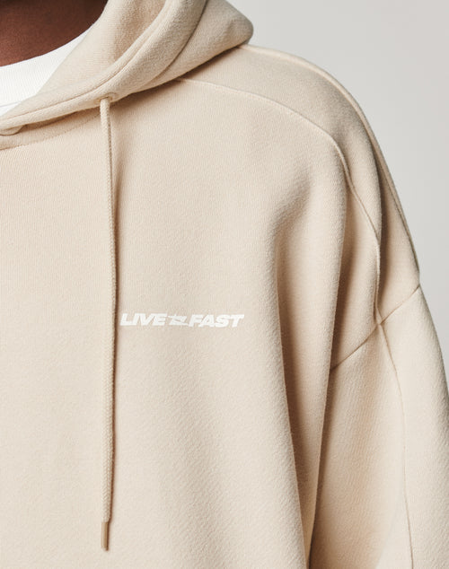 A close-up of the LFDY Pleated Hooded Zip by LIVE FAST DIE YOUNG in beige Baumwolle, Oversize Fit, with a drawstring hood and LIVE FAST in white on the chest.