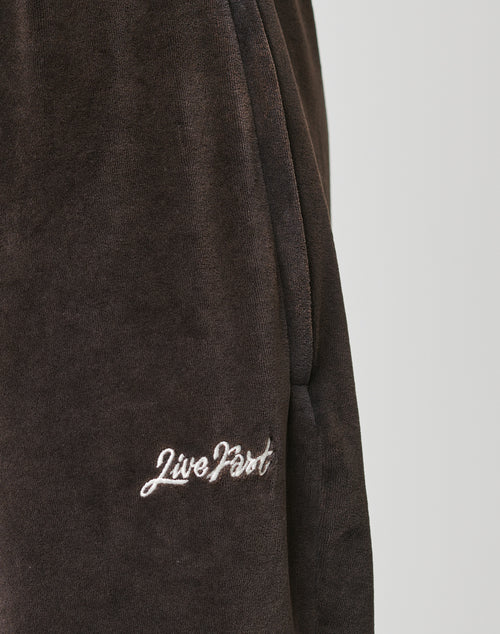 Close-up of LFDY Velour Pants by LIVE FAST DIE YOUNG in dark brown velour, featuring an elastic waistband and Live Fast white embroidery near the pocket. Made from a cotton-polyester blend for lasting comfort.