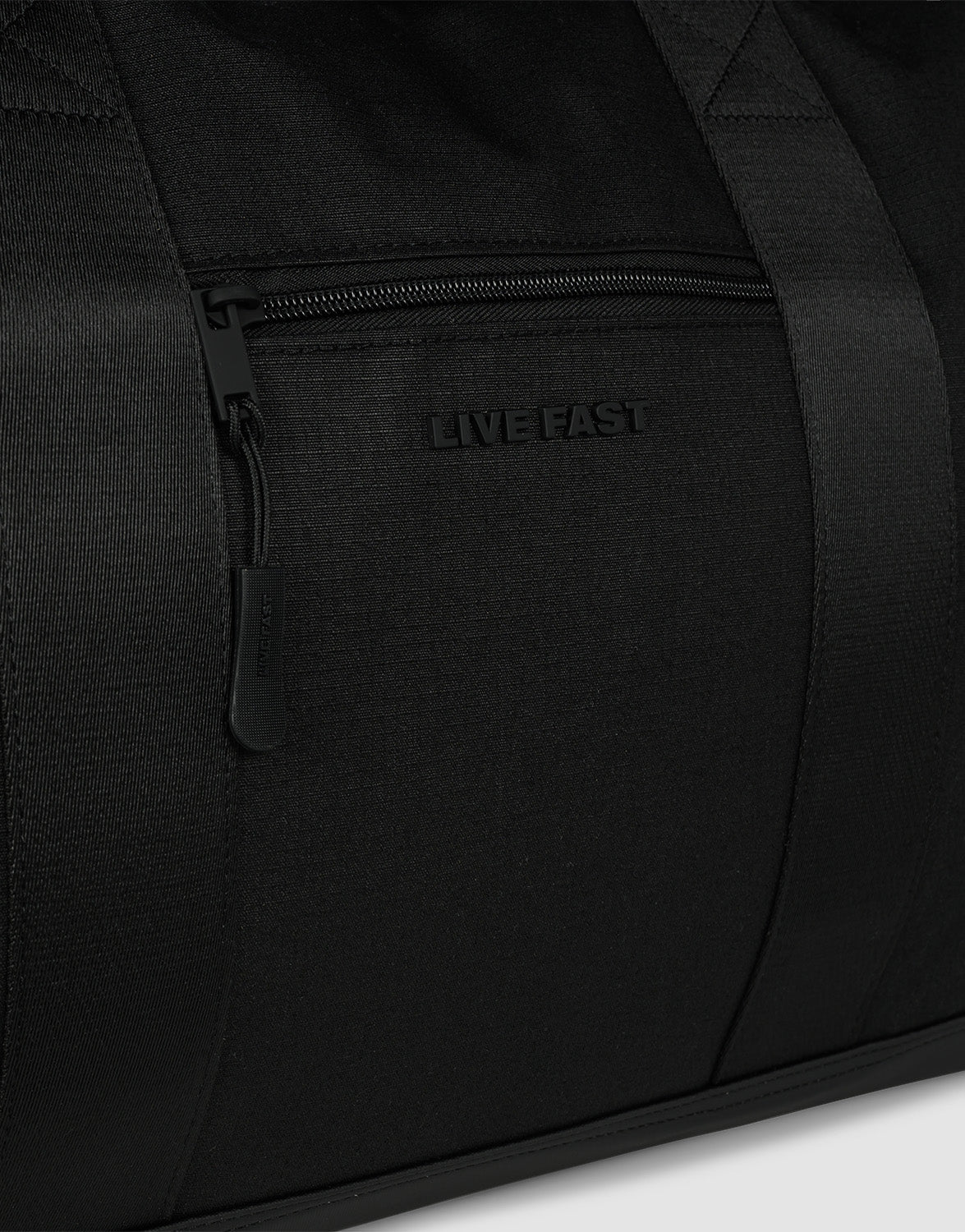 Close-up of the black LFDY Weekender 60 by LIVE FAST DIE YOUNG, a 60L Sporttasche featuring a zippered pocket, "LIVE FAST" embossed above the zipper, durable fabric, smooth stitching, and an abnehmbarer Schultergurt for minimalist style.